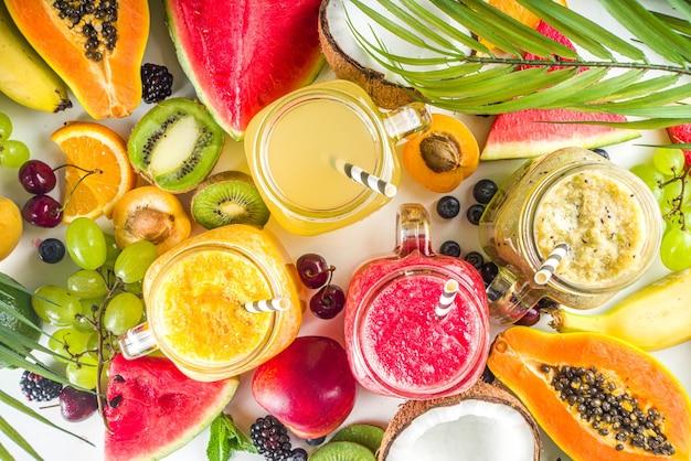 Assorted different fruit smoothies and juices with tropical fresh fruits and berries Clean eating healthy lifestyle diet and vitamin drink beverages concept Top view flatlay white table background