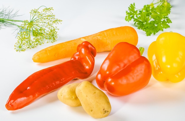 Assorted fresh vegetables paprika carrots potatoes and greens on a white background