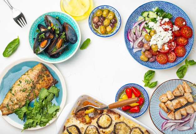 Assorted Greek dishes on white stone background from above, moussaka, grilled fish, souvlaki, greek salad, steamed mussels with herbs, appetizers of Greece from above, space for text