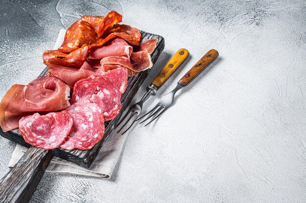 Assorted meat appetizers - salami, jamon, choriso sausages. White background. Top view. Copy space.