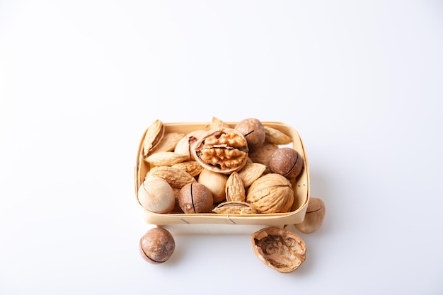 Assorted nuts in the shell on a white background walnuts pecans almonds macadamia Nuts in a basket Selective focus closeup Place for text