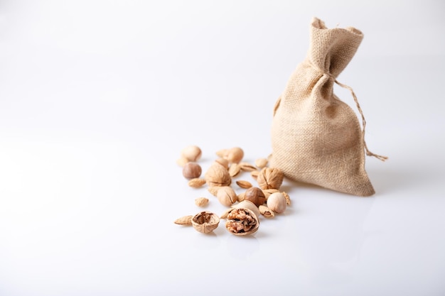 Assorted nuts in the shell on a white background walnuts pecans almonds macadamia Nuts in a burlap bag Selective focus closeup Place for text