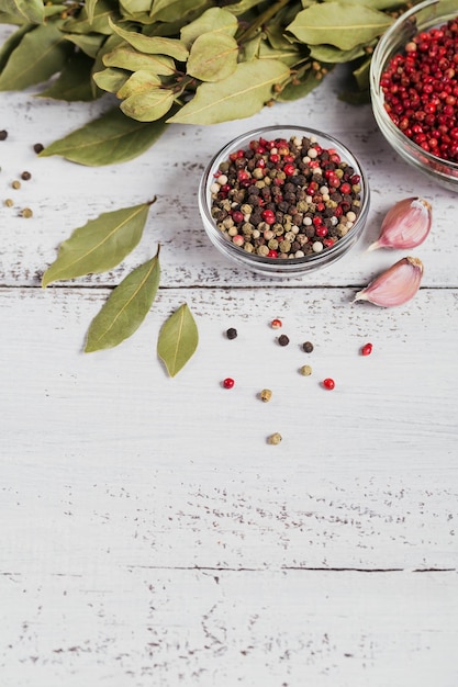 Assorted pepper spices Pepper mix Black red and white peppercorns dried bay laurel leaves and garlic on white wooden background