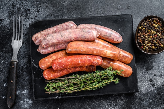 Assorted raw homemade sausages on a stone board. Black background. Top view.