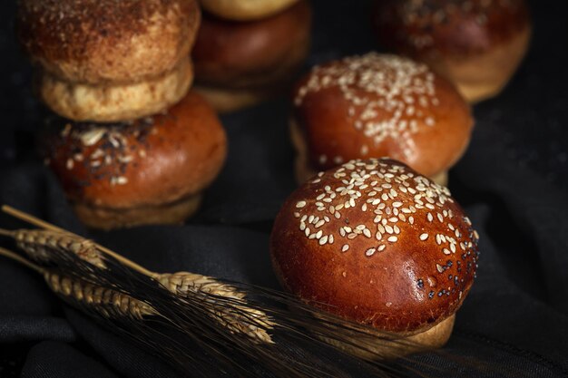 Assorted round homemade brioche buns with seeds on dark background with high contrast light. Isolated