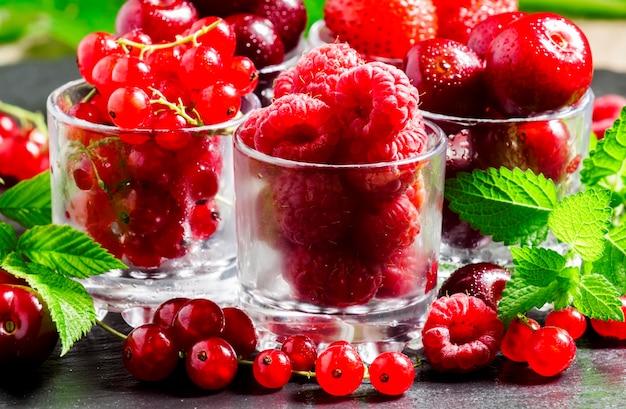 Assorted summer berries raspberries red currant cherry strawberry with glasses on black background selective focus