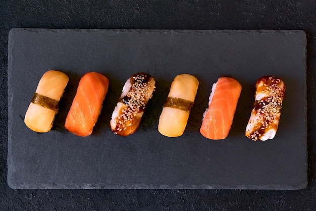 Assorted sushi with salmon eel and escolar on black stone plate on dark background Minimal concept