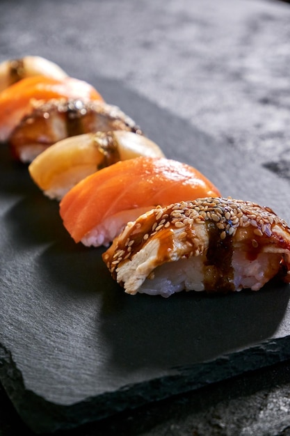 Assorted sushi with salmon eel and escolar on black stone plate on dark background Minimal concept