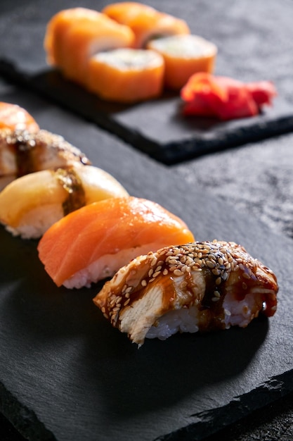 Assorted sushi with salmon eel and escolar on black stone plate on dark background