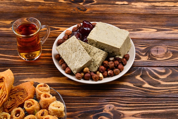 Assorted traditional eastern desserts with tea on wooden background Arabian sweets on wooden table Baklava halva rahat lokum sherbet nuts dates kadayif on plates Space for text