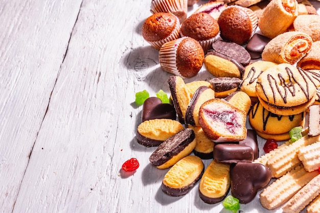 Assorted various cookies and cupcakes. Trendy hard light, dark shadow. White wooden boards background, copy space