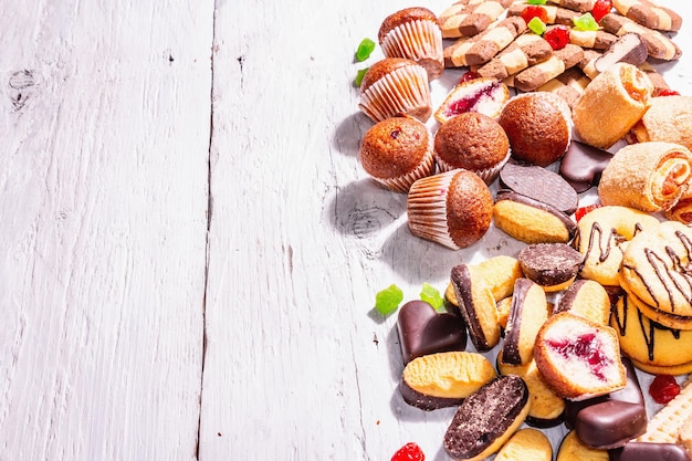 Assorted various cookies and cupcakes. Trendy hard light, dark shadow. White wooden boards background, top view