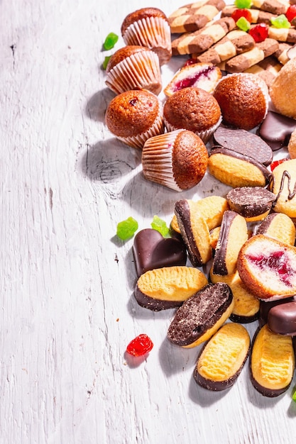 Assorted various cookies and cupcakes. Trendy hard light, dark shadow. White wooden boards background, top view