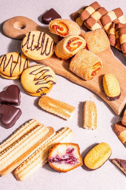 Assorted various cookies and muffins. Fashionable hard light, dark shadow. Stone concrete background, top view