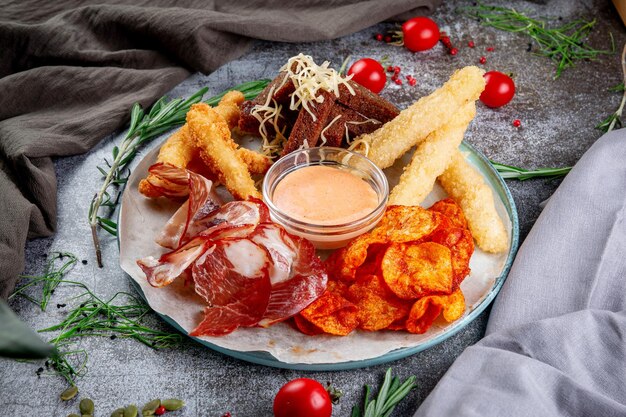 An assortment of beer snacks Fried potato chips cheese and chicken nuggets dried bacon slices gravy and croutons