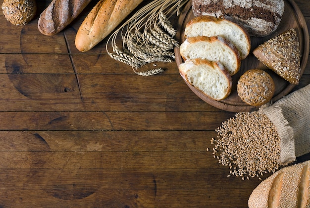 Assortment bread products and small bag with wheat grains on wooden table with copy space for your text. Rustic style, top view