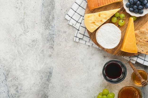 Assortment of cheese honey cracker blueberries grapes with red and white wine in glasses antipasto server on white marble board on grey background Cheese plate Flat lay copy space