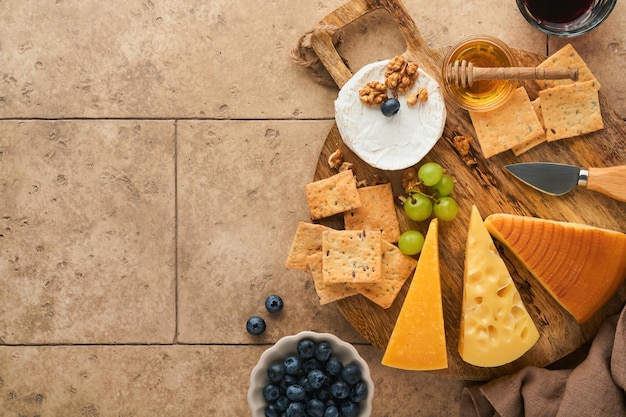 Assortment of cheese honey cracker blueberries grapes with red and white wine in glasses antipasto server on white marble board on grey background Cheese plate Flat lay copy space