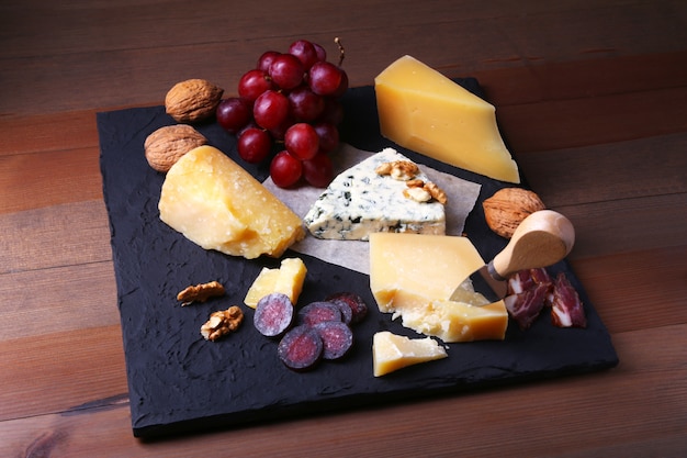 Assortment of cheese with fruits, grapes, nuts and cheese knife on a wooden serving tray.