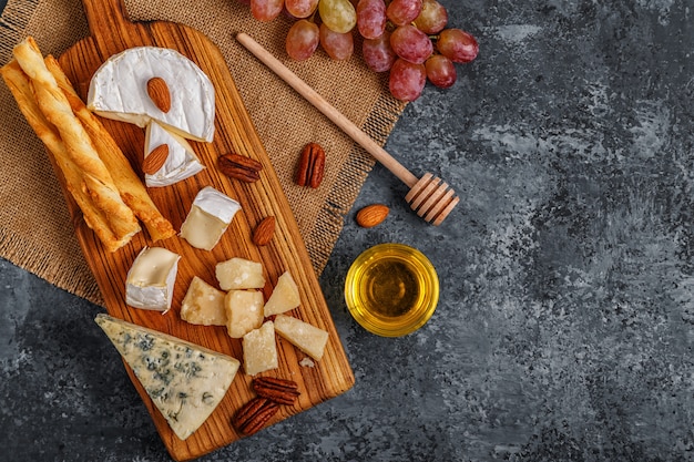 Assortment of cheese with honey, nuts and grape on a cutting board.