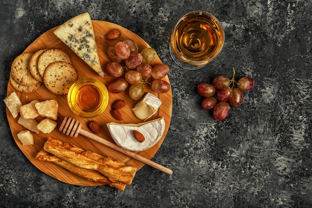 Assortment of cheese with wine, honey, nuts and grape on a cutting board.