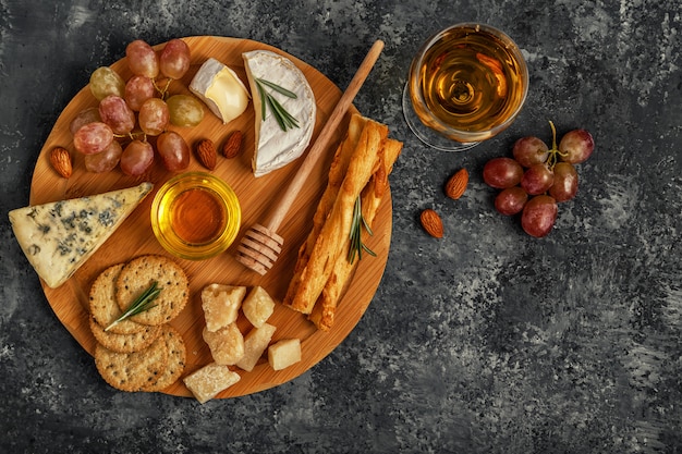 Assortment of cheese with wine, honey, nuts and grape on a cutting board.