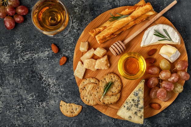 Assortment of cheese with wine, honey, nuts and grape on a cutting board.