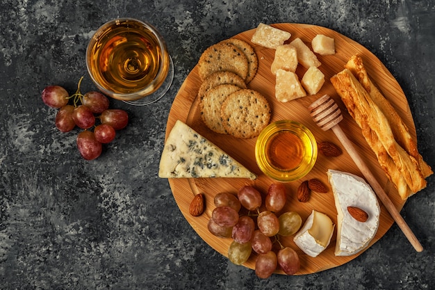 Assortment of cheese with wine, honey, nuts and grape on a cutting board.