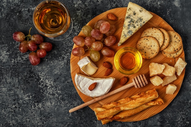 Assortment of cheese with wine, honey, nuts and grape on a cutting board