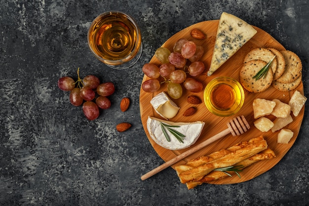 Assortment of cheese with wine, honey, nuts and grape on a cutting board