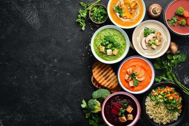 Assortment of colored vegetable cream soups. Dietary food. On a black stone background. Top view. Free copy space.