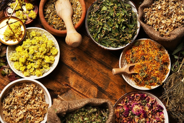 Assortment of dry medicinal herbs in bowls on wooden background top view