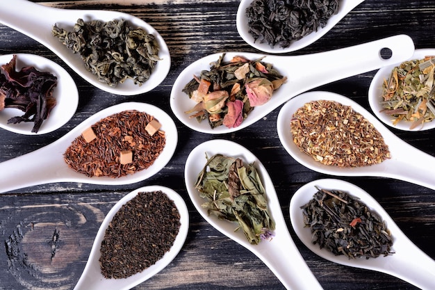 assortment of dry tea in ceramic bowls on wooden background