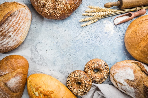 Assortment of fresh baked bread and buns on stone background, top view