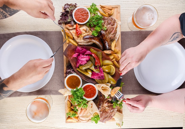 Assortment of fried meat, potatoes, sausages, pickles, tomatoes, peppers, herbs, lavash on a wooden tray on the table. Top view.