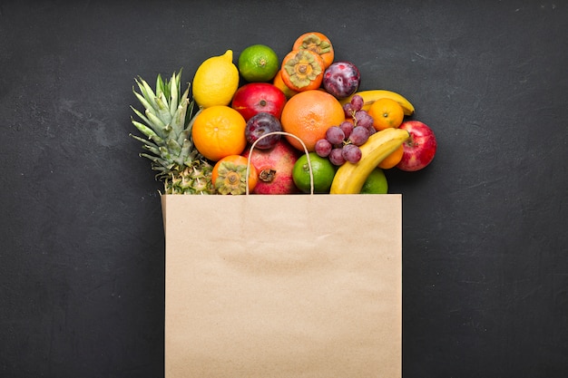 Assortment of fruits in a paper bag on black concrete. concept of vitamins in human diet.