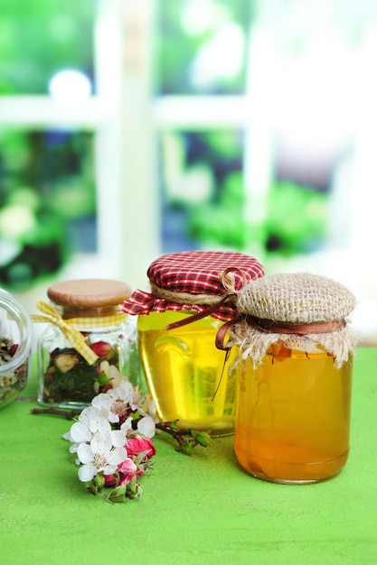 Assortment of herbs and tea and honey in glass jars on wooden table on bright background