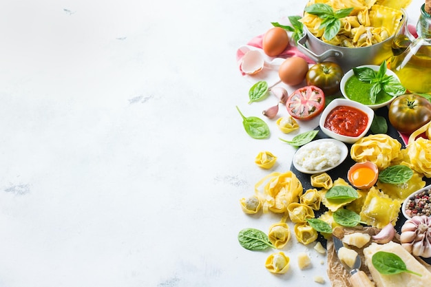 Assortment of italian food and ingredients ravioli with ricotta and spinach pasta spaghetti pesto tomato sauce olive oil parmesan cheese Copy space background