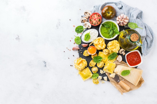 Assortment of italian food and ingredients ravioli with ricotta and spinach pasta tortellini pesto tomato sauce olive oil parmesan cheese Top view flat lay copy space background