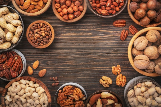 Assortment of nuts in bowls Cashews hazelnuts walnuts pistachios pecans pine nuts peanuts macadamia almonds brazil nuts Food mix on wooden background top view copy space