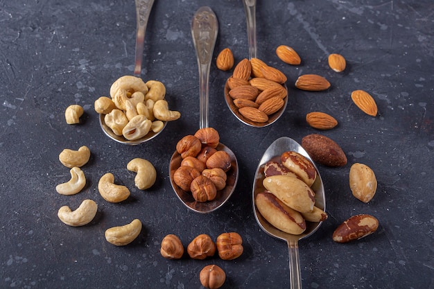 Assortment of nuts cashew, hazelnuts, almonds, brazil nuts on metal silver spoons . Healthy vegetarian snacks.