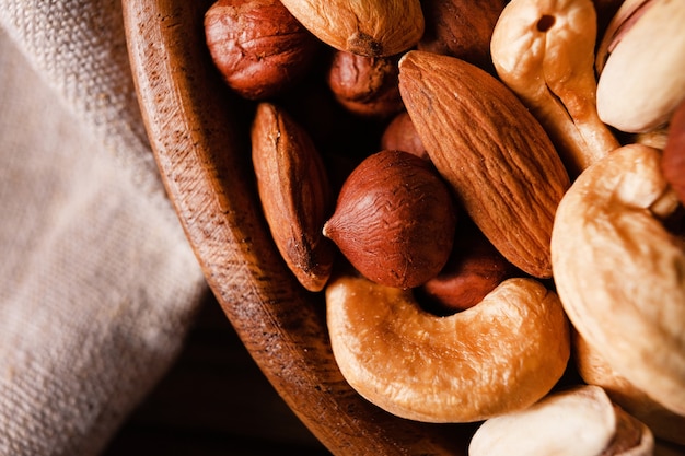 Assortment of nuts in wooden bowl on dark wooden table. Cashew, hazelnuts, almonds and pistachios.