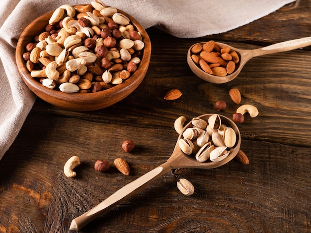 Assortment of nuts in wooden bowl on dark wooden table. Cashew, hazelnuts, almonds and pistachios.