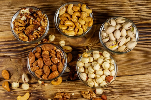 Assortment of nuts on wooden table Almond hazelnut pistachio walnut and cashew in glass bowls Top view Healthy eating concept