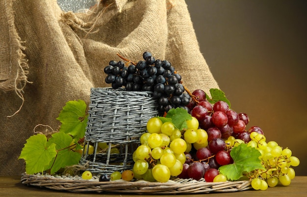 Assortment of ripe sweet grapes in basket on brown background