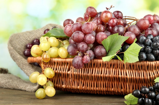 Assortment of ripe sweet grapes in basket on green background