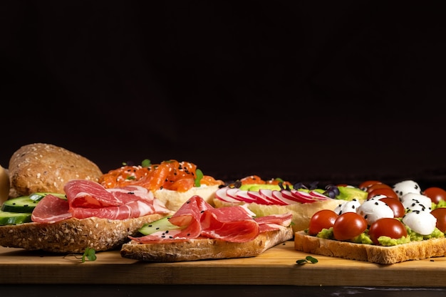 An assortment of sandwiches with fish, cheese, meat and vegetables lay on the board and a bun