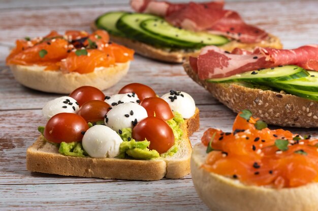 An assortment of sandwiches with fish, cheese, meat and vegetables lay on the wooden table