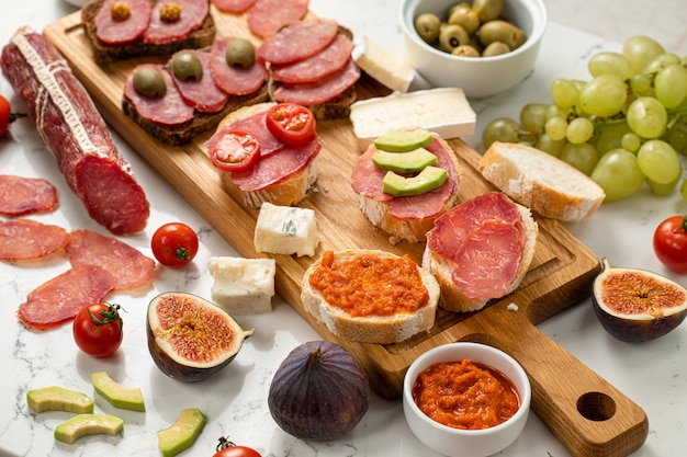 Assortment of sausages and cheese, salami camembert brie, grapes, baguette slices, olives, on white stone background. Appetizers table with antipasti snacks. White marble background. Close up