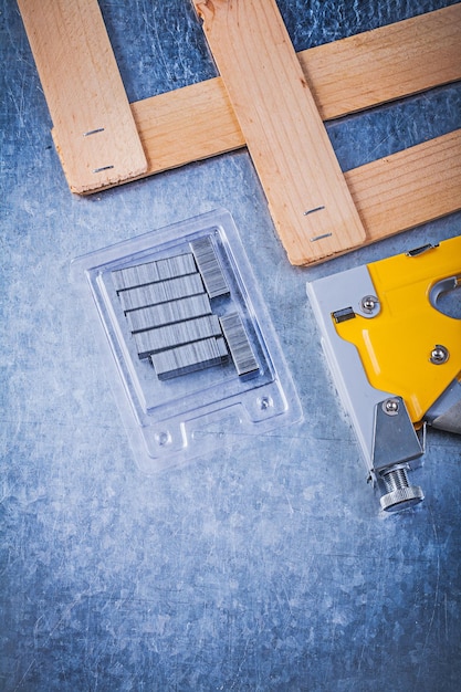 Assortment of stapler gun metal staples wooden plank on metallic background construction concept